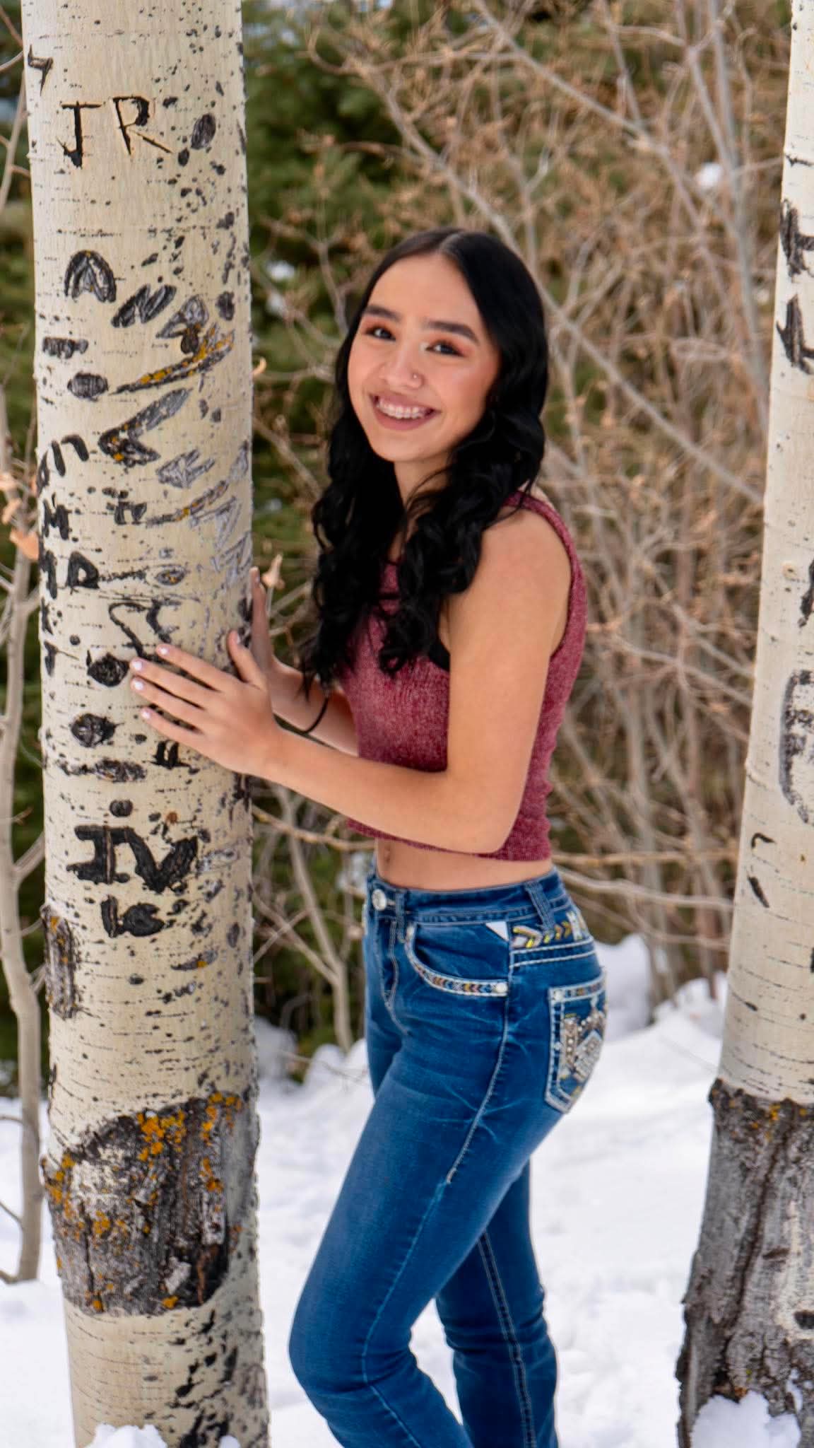 Senior portrait beside an aspen tree carved with initials, snow