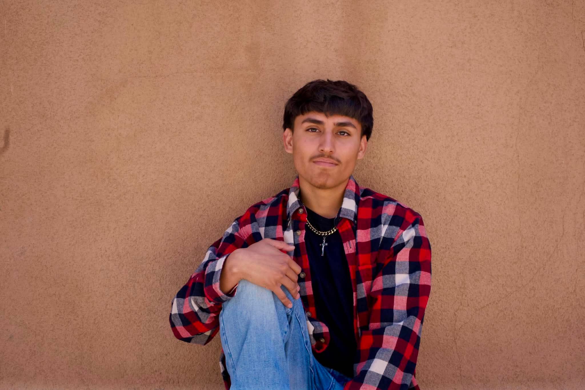 Senior portrait in flannel against an adobe wall