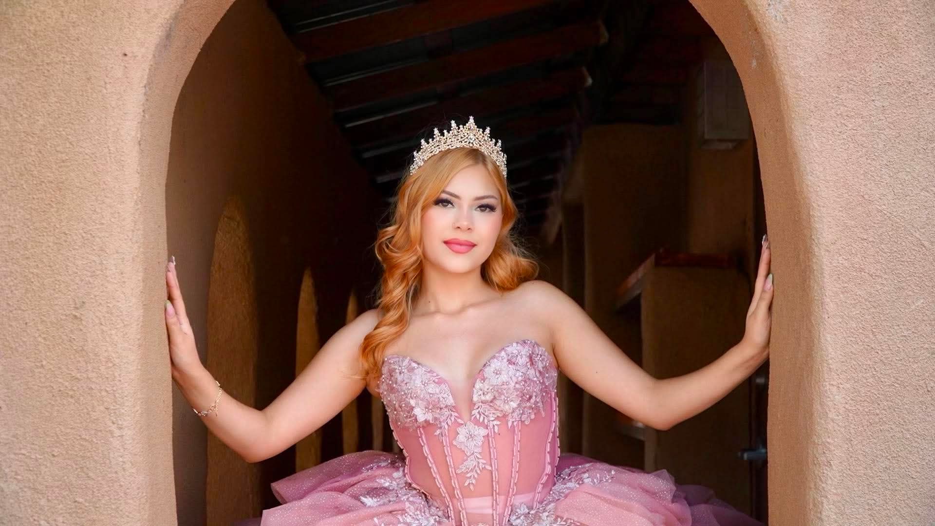 Quinceañera in a pink gown and tiara under an adobe archway